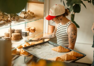 A pastry chef in a bakery arranges croissants, showcasing an inviting display of cookies and croissants.